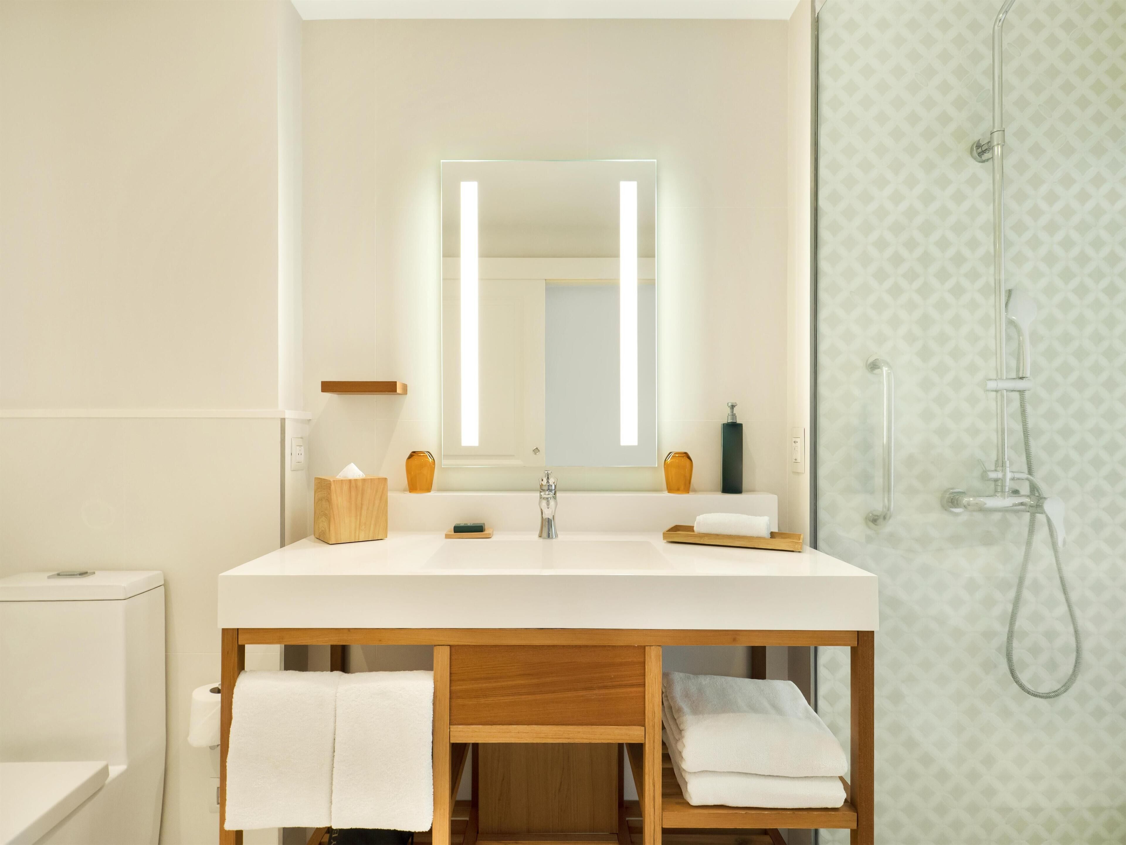 A modern bathroom with a large mirror, a wooden vanity, a shower, and a toilet.