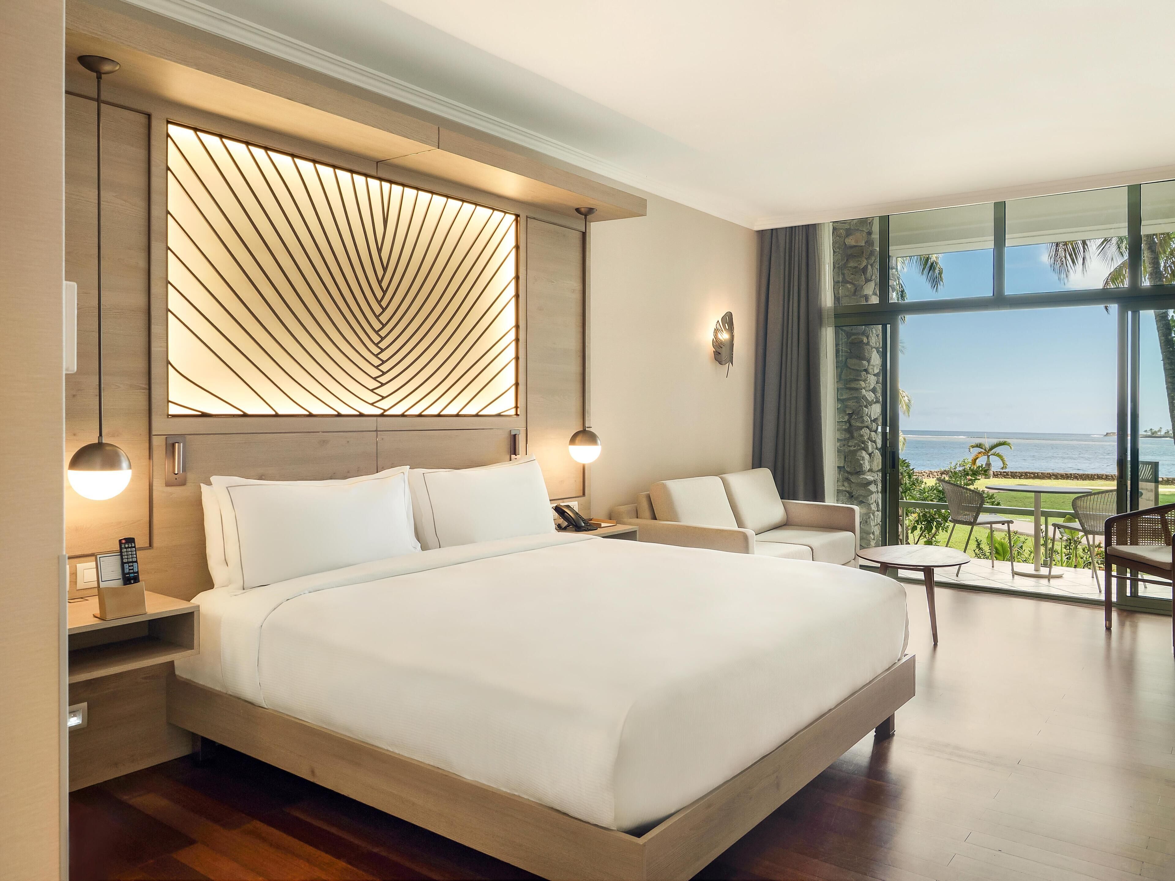 A modern hotel room with a large bed, a seating area, and a view of the ocean.