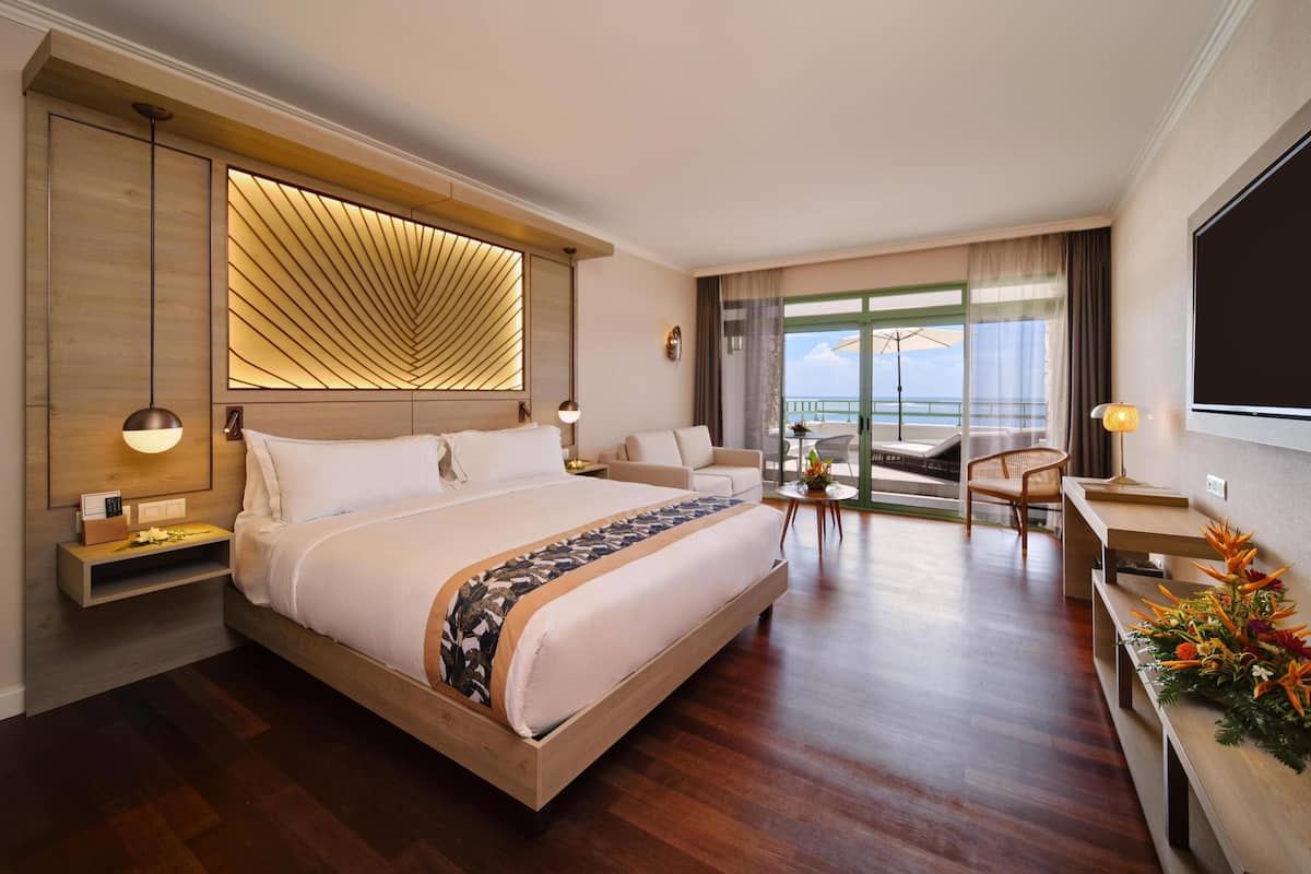 A modern hotel room with a large bed, a desk, a chair, and a balcony with a view.