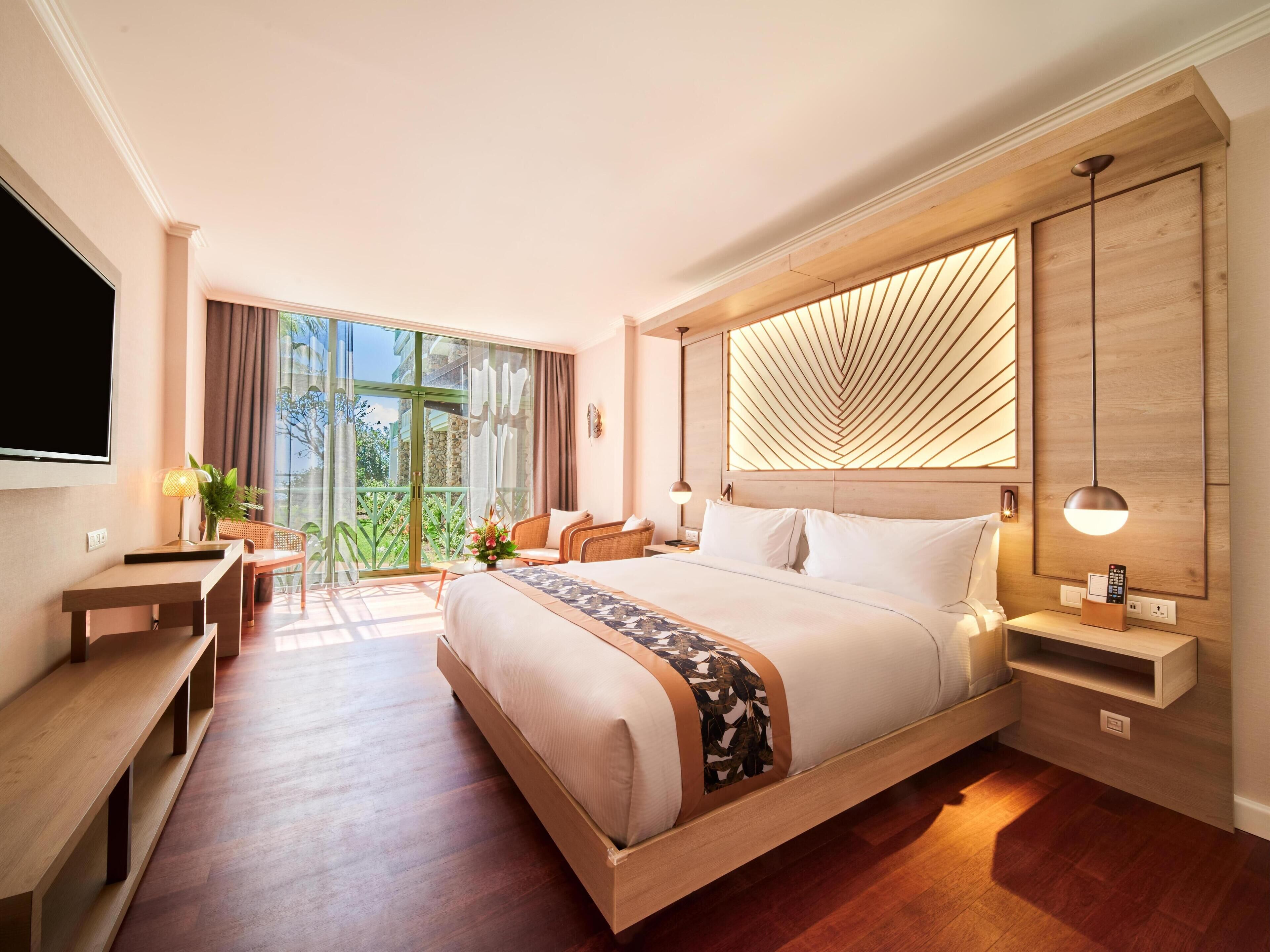 A modern hotel room with a large bed, a desk, a chair, and a TV.