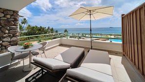 A balcony with a view of the ocean, a lounge area with a table and chairs, and a large umbrella.
