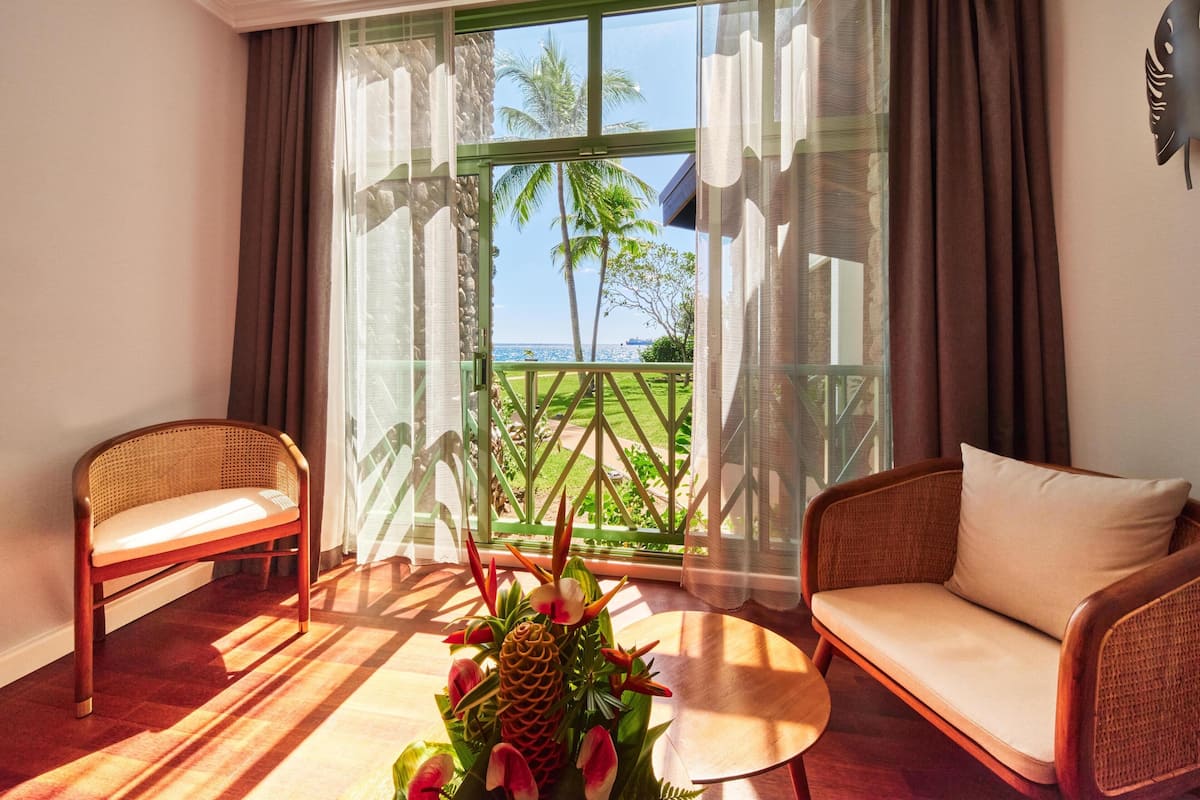 A room with a large window, two wicker chairs, a small round table, and a tropical plant arrangement.