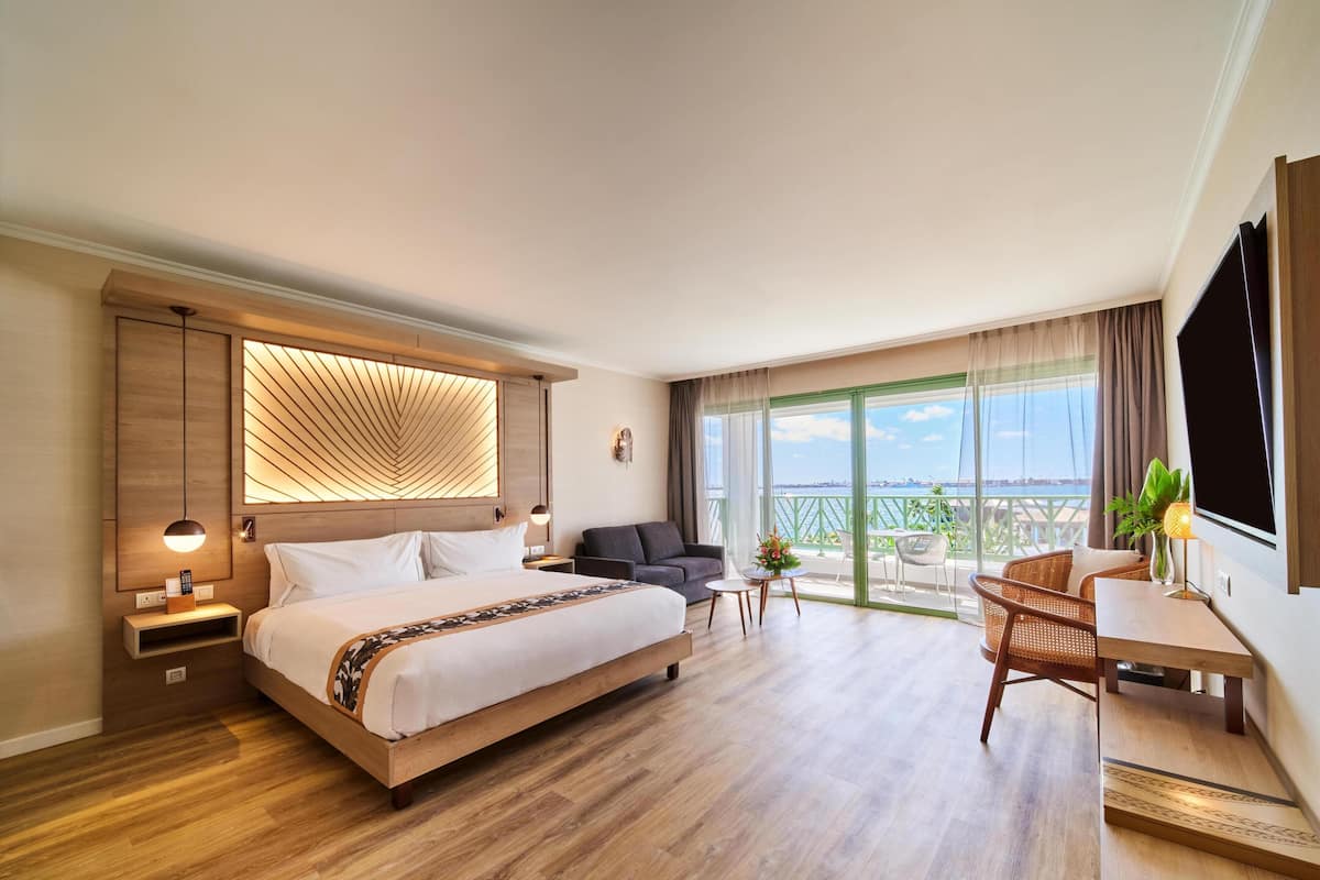 A modern hotel room with a large bed, a seating area, and a balcony with a view.
