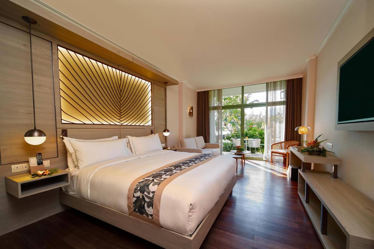 A modern hotel room with a large bed, bedside tables, a desk, and a view of the outdoors.