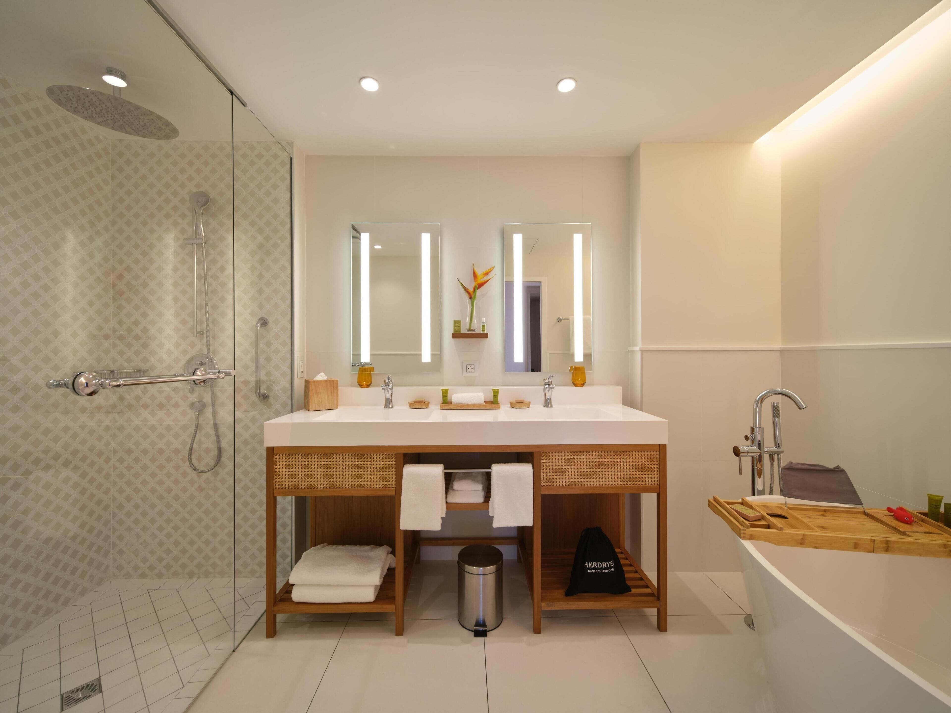 A modern bathroom with a glass shower enclosure, a large vanity with a mirror, and a separate bathtub area.