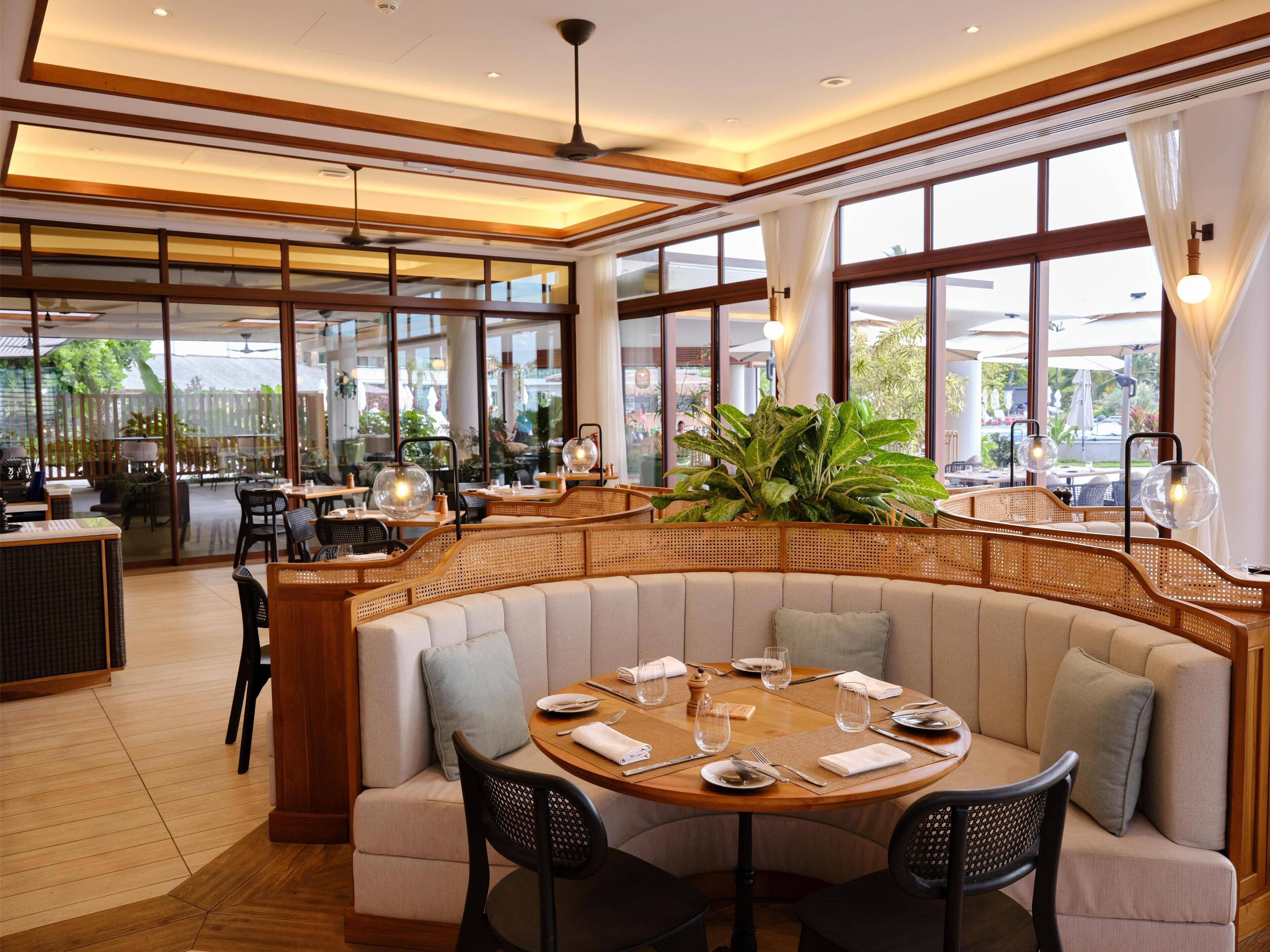 A restaurant with a round table set for dining, cushioned seating, and large windows offering a view of the outdoors.