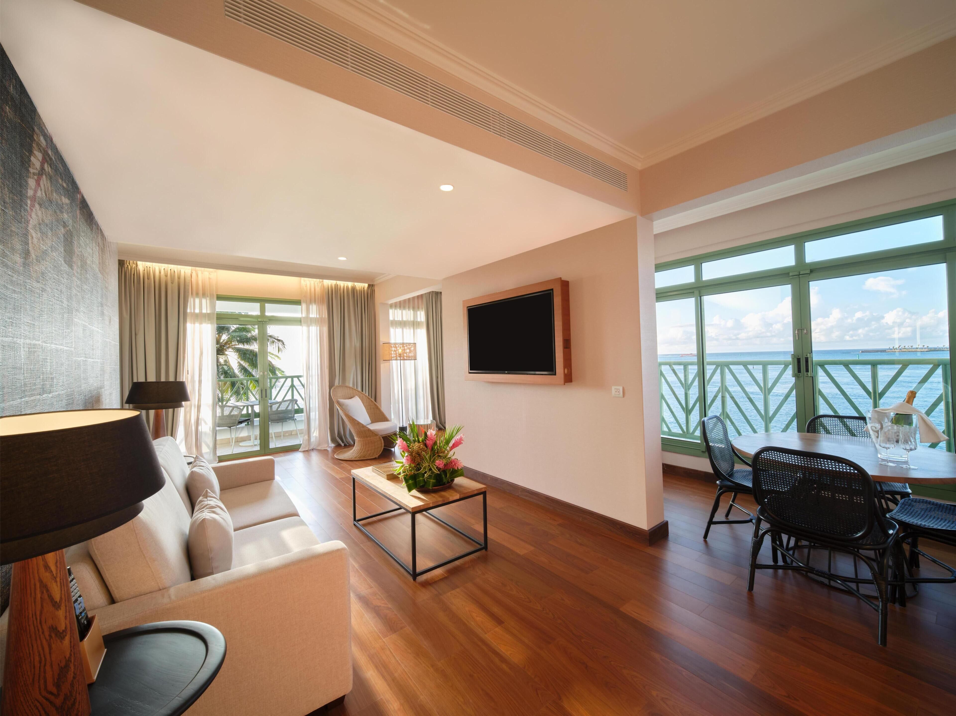 Amplia sala de estar con un sofá, una mesa de centro con flores, un televisor y un balcón con vista al mar.