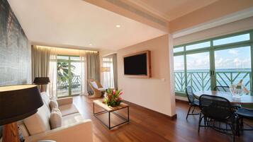 Amplia sala de estar con un sofá, una mesa de centro con flores, un televisor y un balcón con vista al mar.