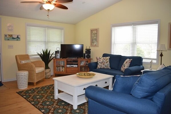 A living room with a blue sofa, a white coffee table, a television, and a ceiling fan.