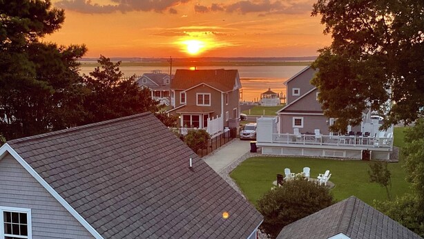 A residential area with houses, a lawn, and a sunset over a body of water. - Allowaves- Luxury Town Home with Community Pool & Fishing Pier (Chincoteague)