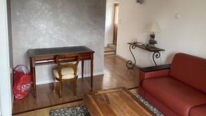 Una sala de estar con un escritorio de madera, un sofá rojo y una lámpara sobre una mesita auxiliar.