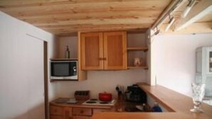 Cocina compacta con muebles de madera, microondas, refrigerador pequeño y encimera de madera.