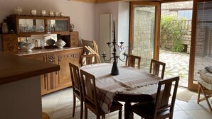 Un comedor acogedor con una mesa de madera, sillas y una araña. Se ve una cocina con armarios y un espejo al fondo.