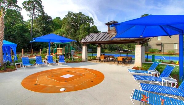 A poolside area with blue lounge chairs, umbrellas, and a covered seating area.