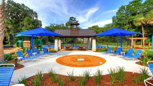 Een overdekt terras met blauwe parasols, een vuurkuil in het midden en een speeltuin op de achtergrond.