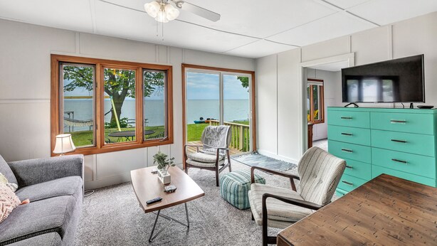 A spacious living area with large windows, a ceiling fan, a teal dresser, and a television. - Turquoise Beach Cottage (Luxemburg)