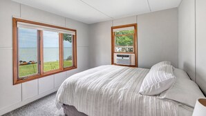 A bedroom with a large window, a bed with striped bedding, and a wall-mounted air conditioning unit. - Turquoise Beach Cottage (Luxemburg)