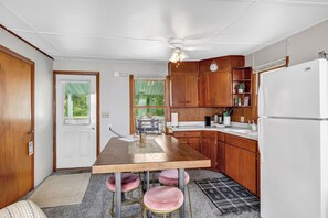 A compact kitchen with wooden cabinets, a white refrigerator, a central island with stools, and a ceiling fan. - Turquoise Beach Cottage (Luxemburg)