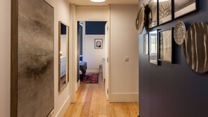 A hallway with wooden flooring, a door leading to a bedroom, and a wall decorated with framed artwork and a mirror. - FLH Amazing Praça Comércio Design Flat (Lisbon)
