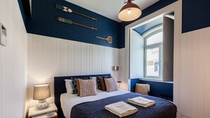 A bedroom with a bed, pillows, a nightstand with a lamp, and a window with a view. - FLH Amazing Praça Comércio Design Flat (Lisbon)