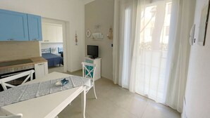 A small, bright room with a kitchenette, a bed, a TV, and a window with curtains. - Apartment Giglio near the sea (Marina di Grosseto)