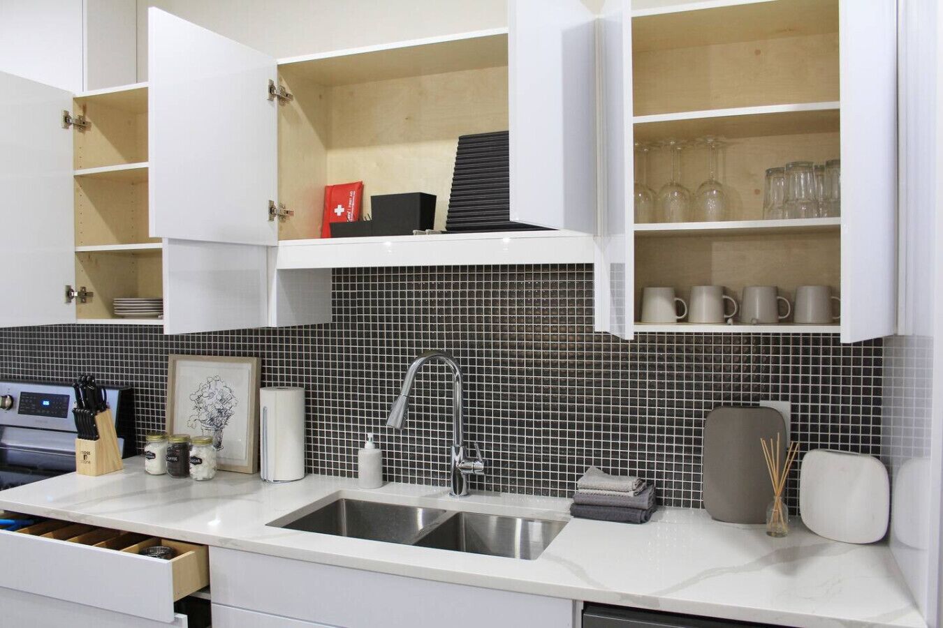 Una cocina moderna con armarios blancos, un salpicadero de azulejos negros y un lavamanos de acero inoxidable.