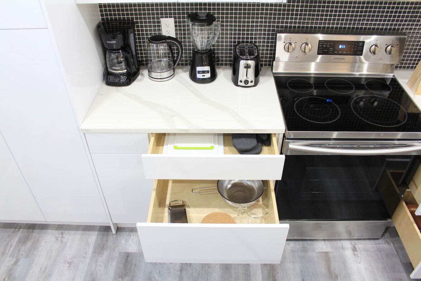 A kitchen with a white countertop, a stainless steel stove, and a drawer with kitchen utensils.
