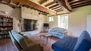 A rustic living room with a stone fireplace, a sofa, a television, and a bookshelf. - Manoir le Cosquer (Pommerit-le-Vicomte)