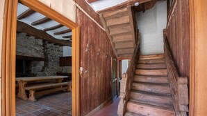 A rustic wooden staircase leading to a stone-walled kitchen area with a wooden bench and a stone fireplace. - Manoir le Cosquer (Pommerit-le-Vicomte)