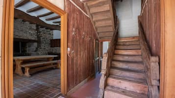 Una escalera de madera rústica que conduce a una zona de cocina con paredes de piedra, un banco de madera y una chimenea de piedra.
