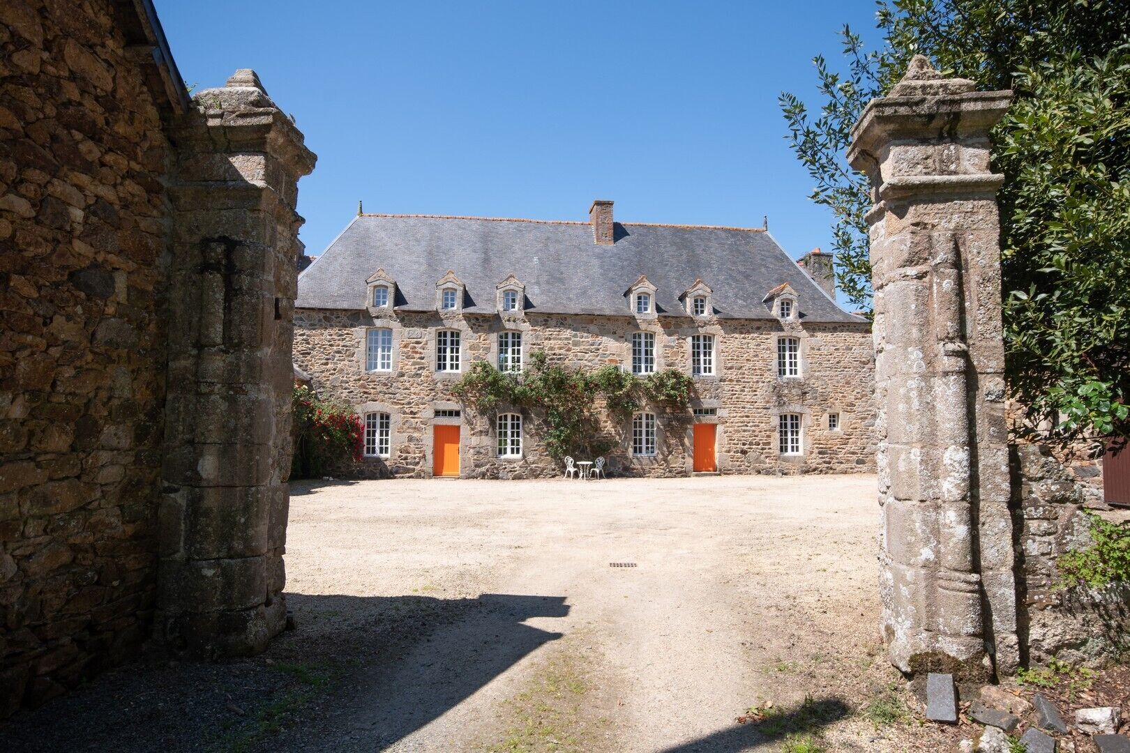 A stone building with a courtyard, featuring a central door and multiple windows.