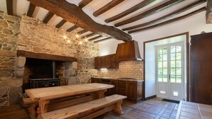 A rustic kitchen with a stone wall, wooden beams, a stone fireplace, and a wooden table. - Manoir le Cosquer (Pommerit-le-Vicomte)