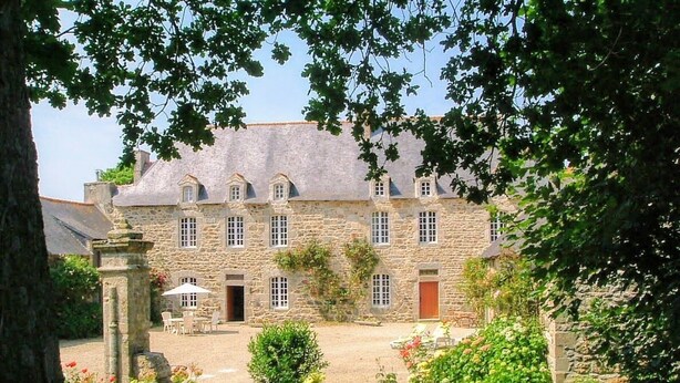 A stone building with a courtyard, surrounded by lush greenery and flowering plants. - Manoir le Cosquer (Pommerit-le-Vicomte)