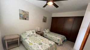 A bedroom with two beds, a nightstand, a ceiling fan, and a wardrobe. - Beachfront Condo with Pool and Ocean View Playa Potrero, Costa Rica (Surfside (Playa Potrero))