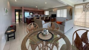 A spacious living area with a round glass table, wicker chairs, and a sofa. A kitchen is visible in the background with modern appliances. - Beachfront Condo with Pool and Ocean View Playa Potrero, Costa Rica (Surfside (Playa Potrero))