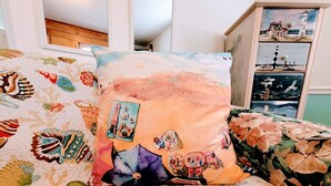 Uma cama com um edredom colorido estampado com criaturas marinhas e uma cena de pôr do sol em uma almofada.