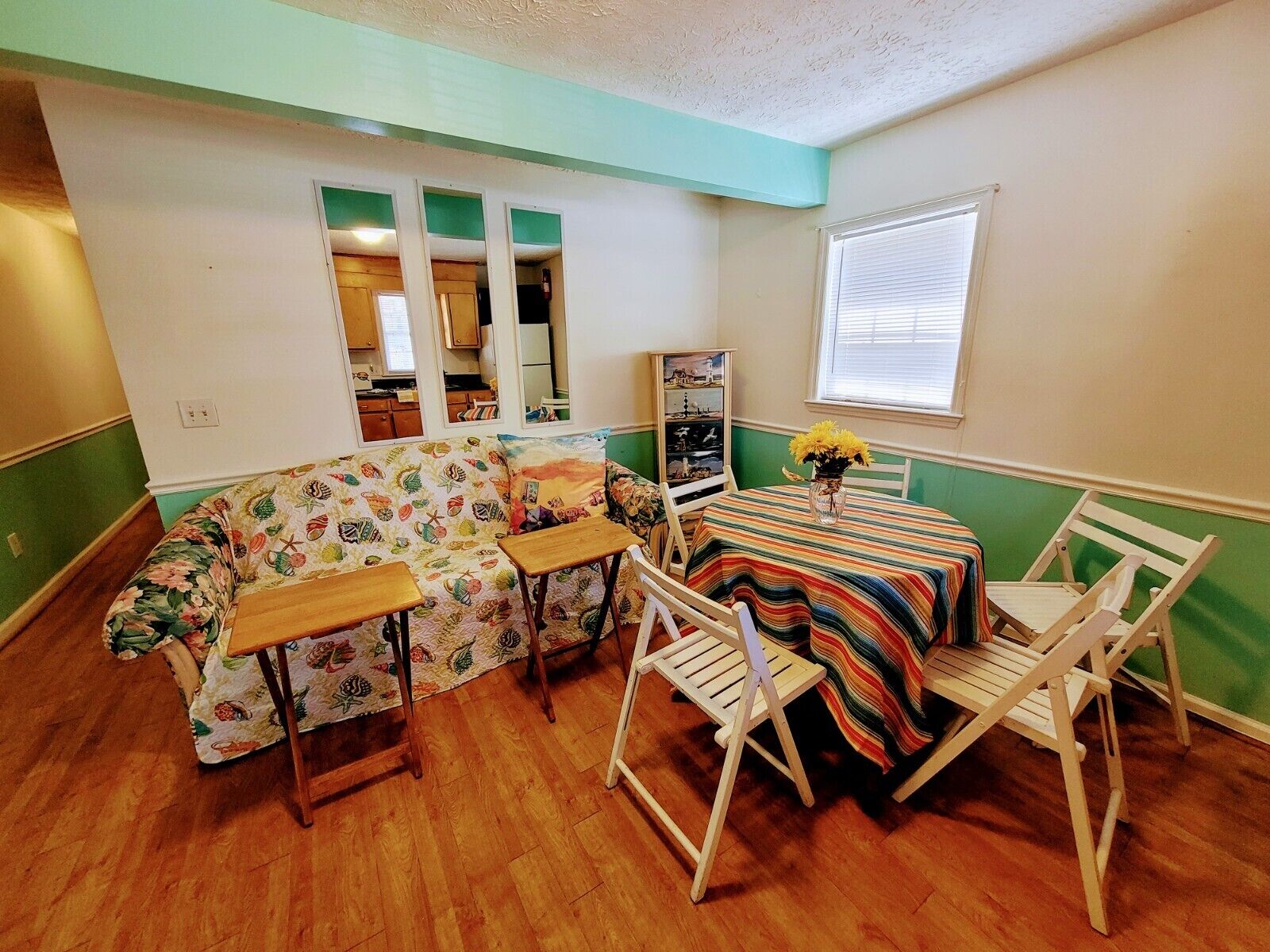 A compact living room with a floral-patterned sofa, a small dining table with a colorful striped tablecloth, and a wooden chair.