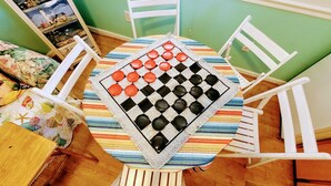 Mesa redonda com um jogo de tabuleiro xadrez, rodeada por cadeiras brancas.