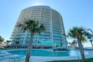 Un hôtel à plusieurs étages, doté d’une façade incurvée, d’une piscine et de palmiers.
