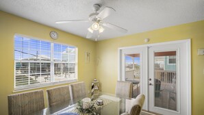 A dining area with a glass table, chairs, a ceiling fan, and a view of the outside through large windows.
