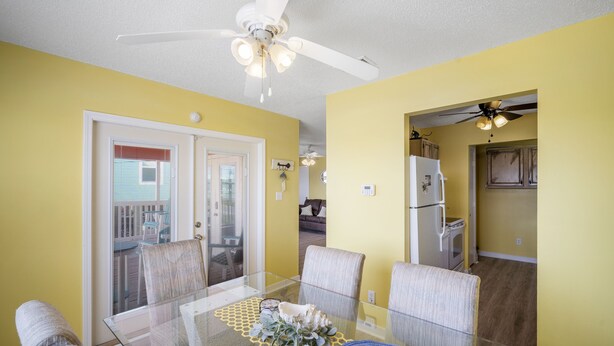 A dining area with a glass table, chairs, and a ceiling fan.