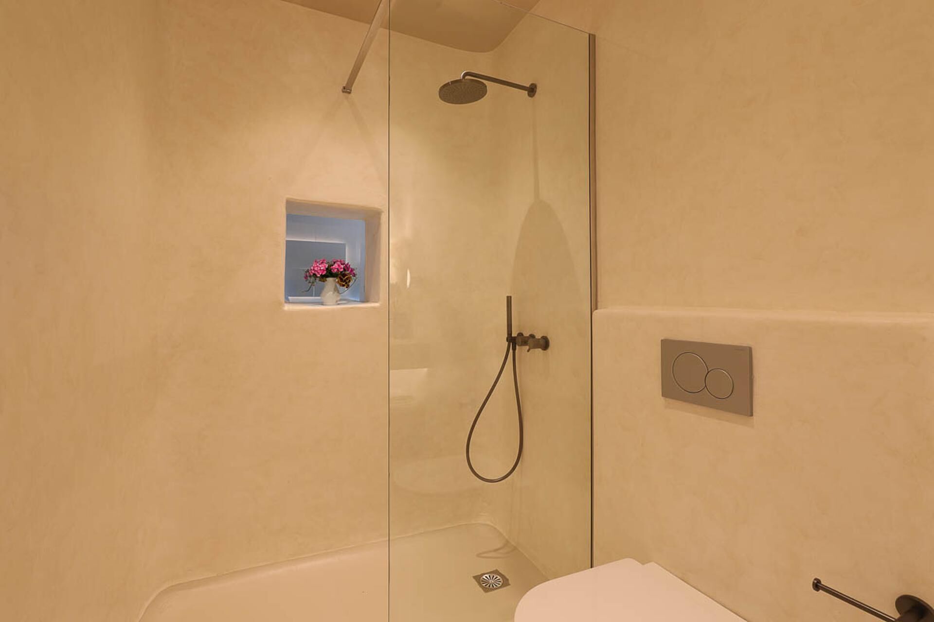 Un baño moderno con ducha envuelta en vidrio, una pequeña ventana con flores y un panel de control a la vista.