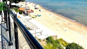 Une vue sur la plage, avec un ciel dégagé, une rive sablonneuse et quelques bateaux sur l’eau.