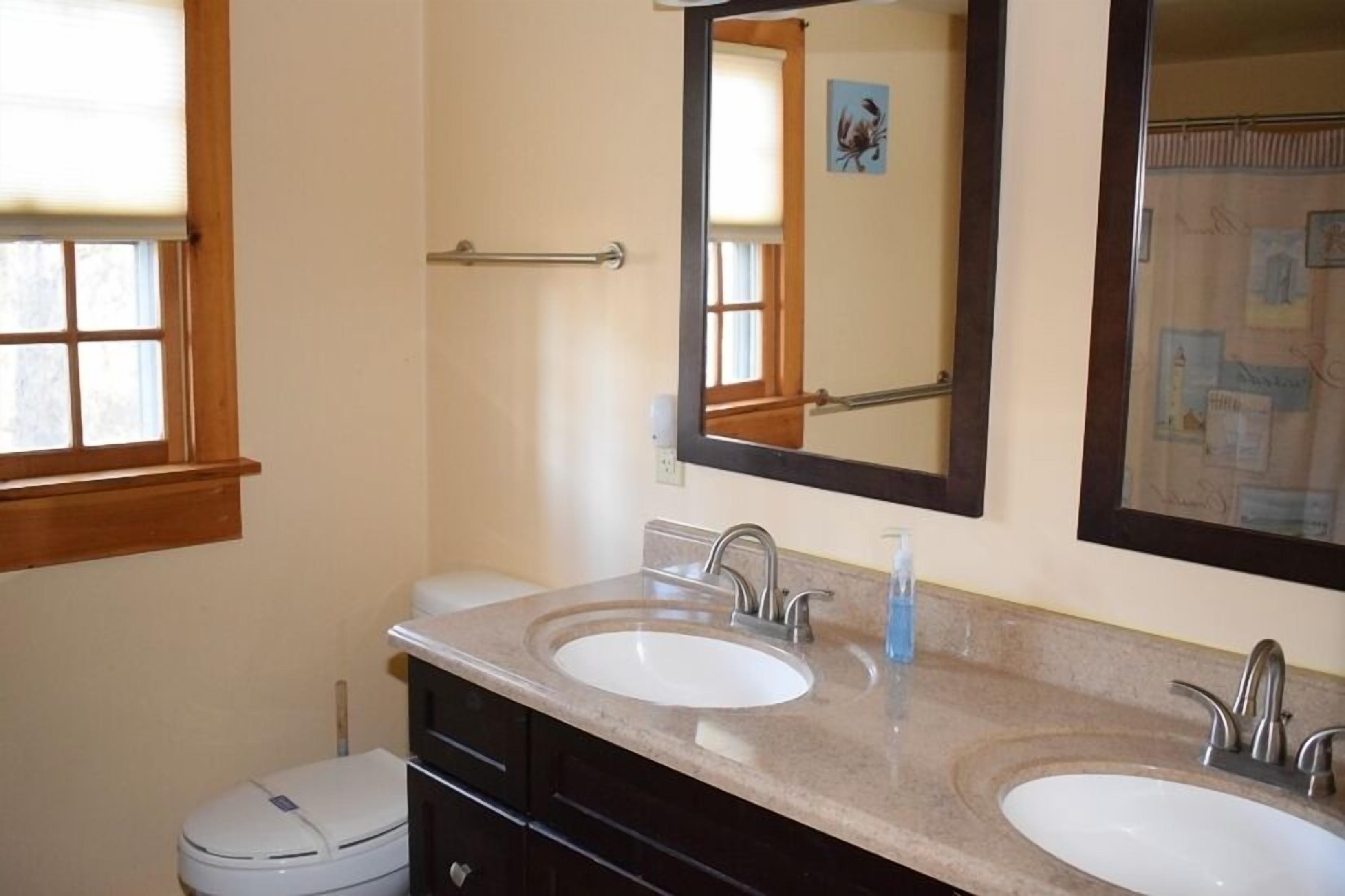 A bathroom with two sinks, a toilet, and a window with blinds.