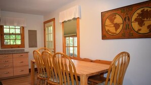A dining room with a wooden table and chairs, a window with a view of greenery, and a painting on the wall. - Aramabad- Close to Beach. Shared Water Access. (Chincoteague)