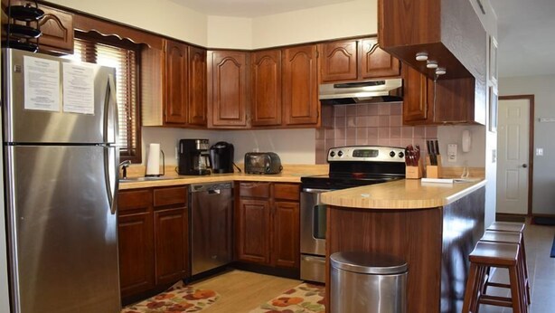 A kitchen with wooden cabinets, stainless steel appliances, a built-in oven, and a small island with stools.