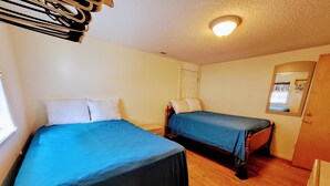 Quarto com duas camas, piso de madeira, luminária no teto e uma porta.