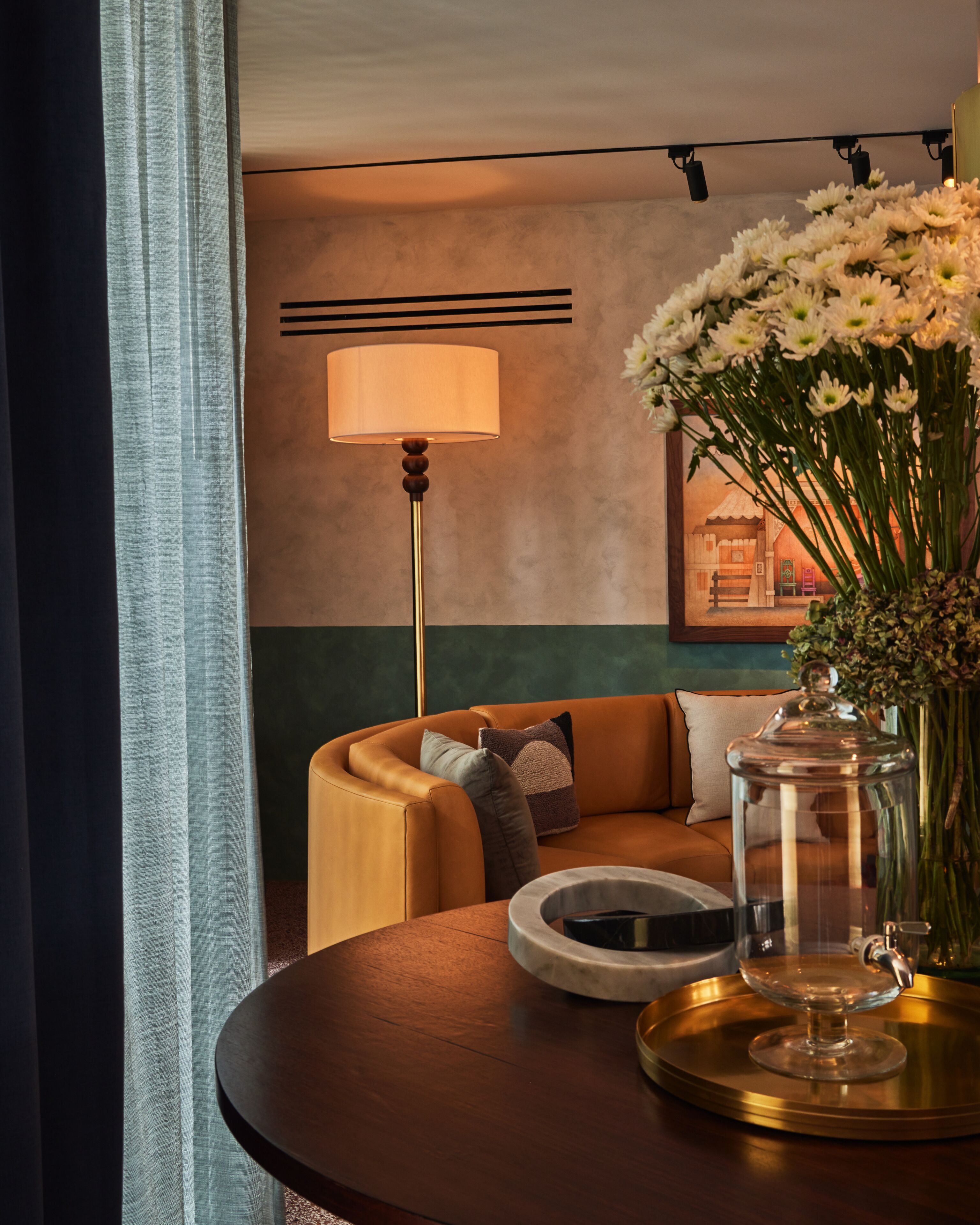 Una habitación acogedora con un sofá de cuero, una mesa redonda con un recipiente de vidrio, una lámpara de pie y un jarrón con flores.