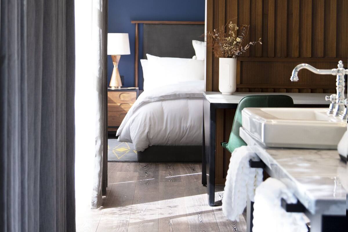 A modern hotel room with a bed, bedside table, lamp, and a large mirror.