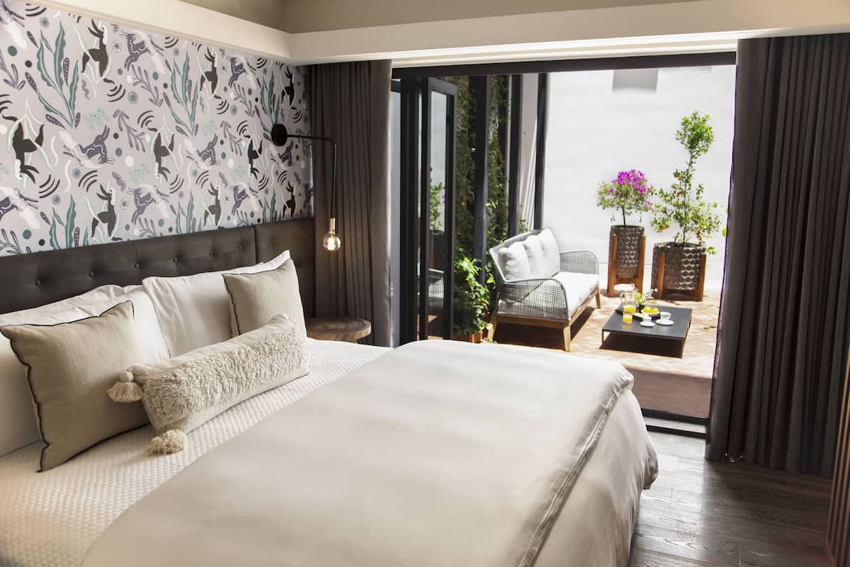 A bedroom with a large bed, a nightstand, a chair, and a table with a plant and a bottle.